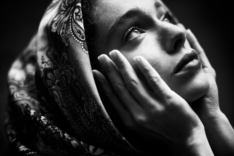 Black and white portrait of a woman in a scarf with delicate facial features and a contemplative gaze. An emotional and atmospheric shot that conveys the inner world of the model.