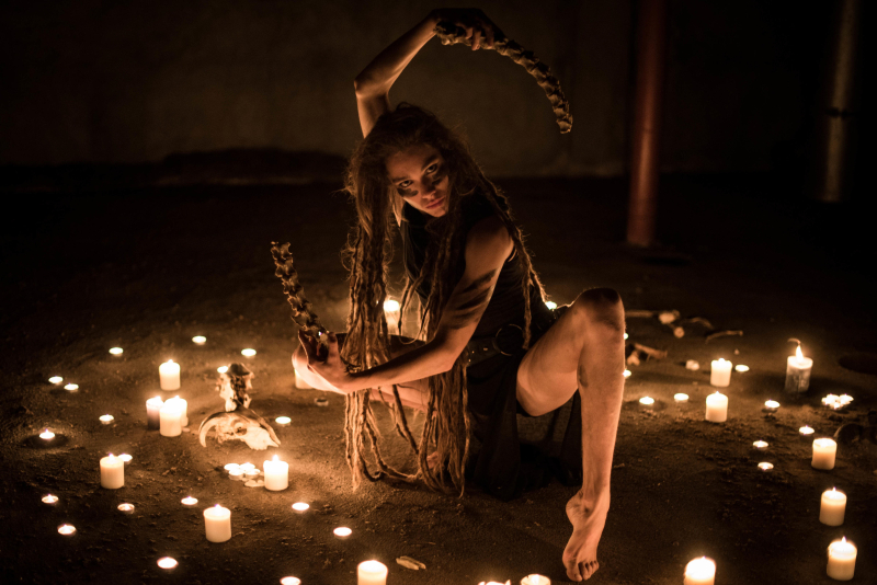Frau führt Ritual mit Kerzen im Dunkeln durch. Mystische Atmosphäre, langes Haar, Zöpfe, Spiritualität, Schamanismus, Geheimnis.
